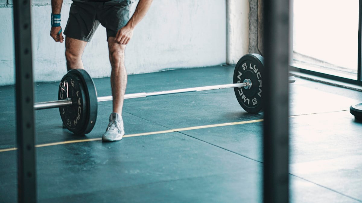 man in black t-shirt and black shorts holding black barbell